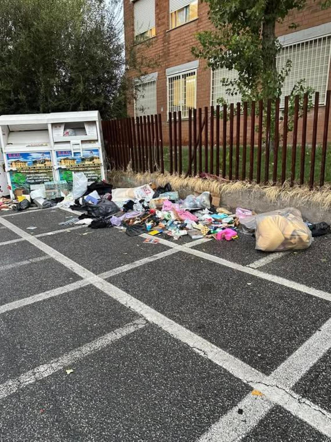 Discarica davanti alla scuola: rifiuti vicino al container per gli abiti usati